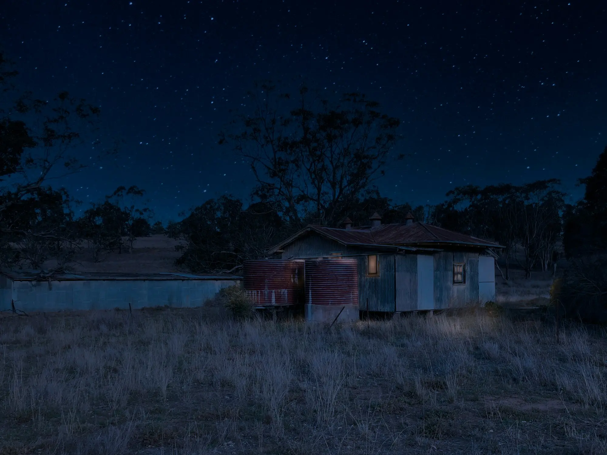 Corrugated iron shed with a rusty water tank under a starry sky among gum trees on a rural Australian property