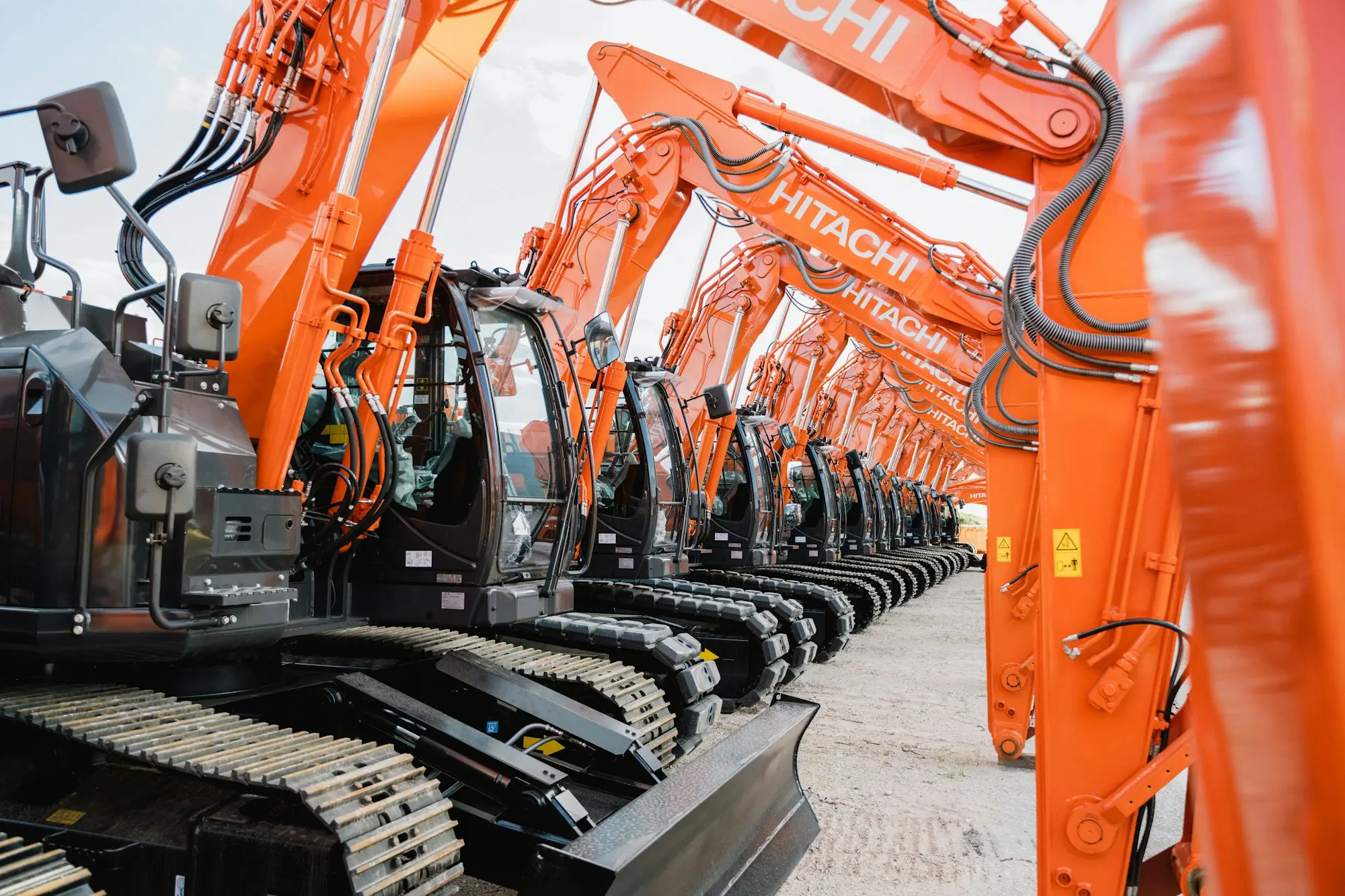 Row of orange tracked excavators lined up on a equipment supplier's yard awaiting delivery
